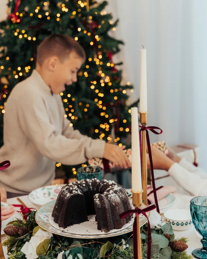 A boy reaching across a laid table, a chocolate bundt cake and tall candles in front of him