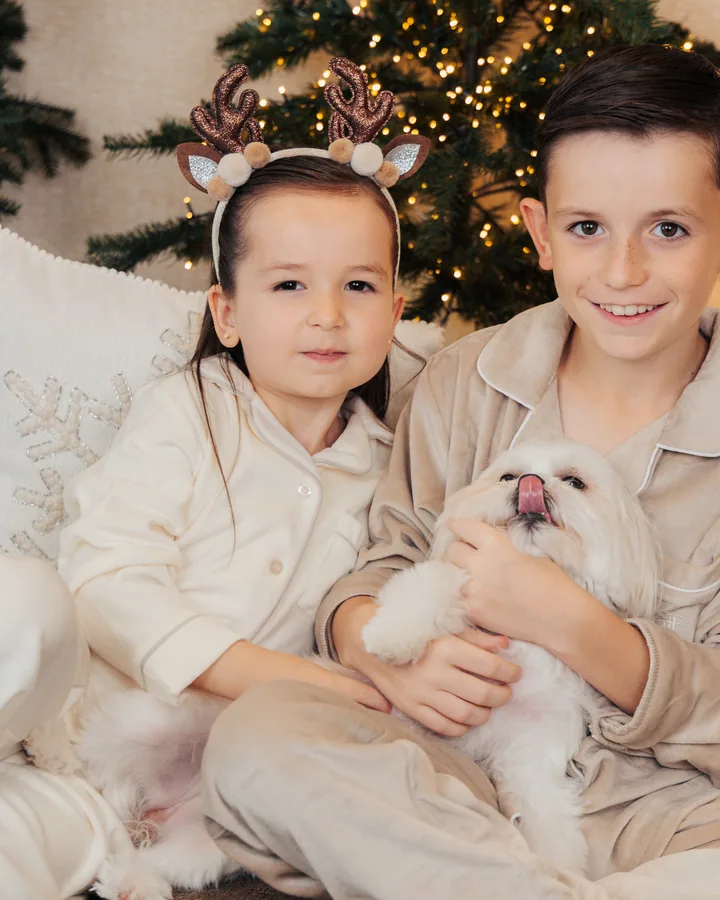 Two boys in cream pyjamas on the sofa holding a small white dog, the tree behind them