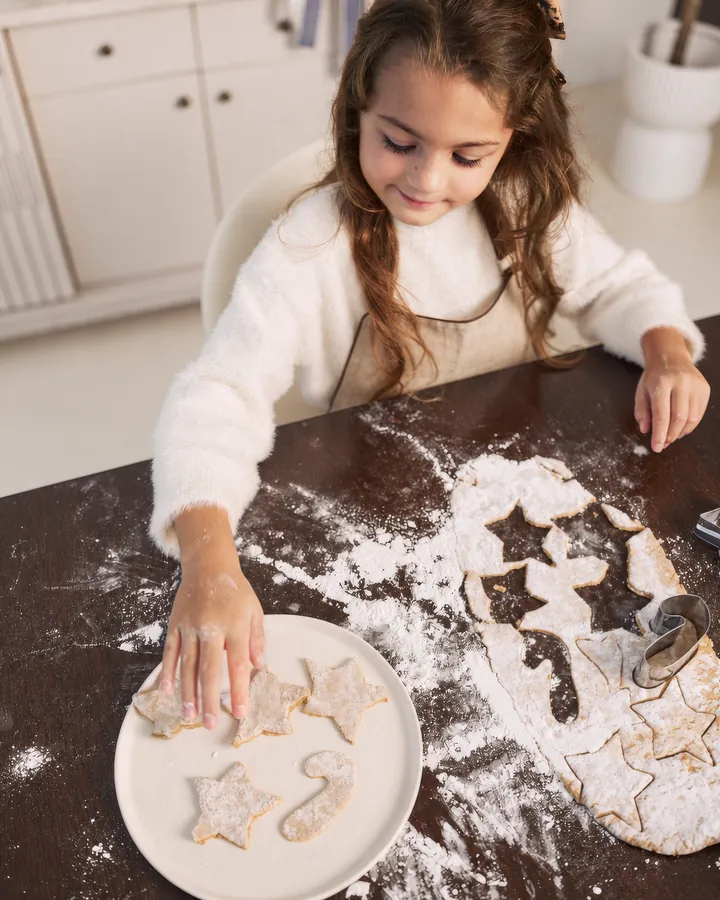 A girl in a cream jumper placing star biscuits on a plate at the floury table