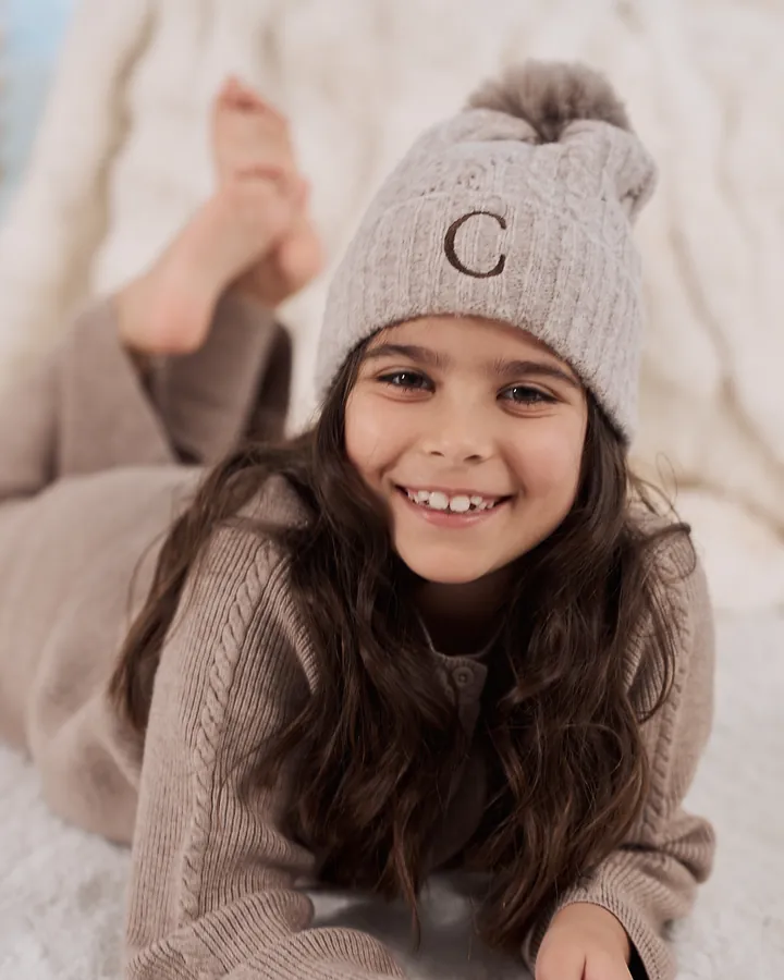 A girl in a knitted hat lying on a soft rug, smiling at the camera