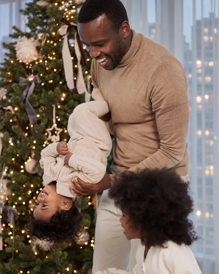 A father lifting his laughing son upside down by the Christmas tree as his daughter looks on