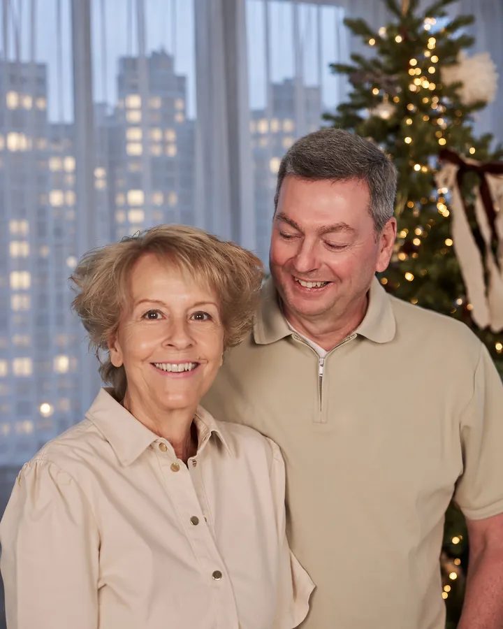 Grandparents smiling together in front of the lit Christmas tree